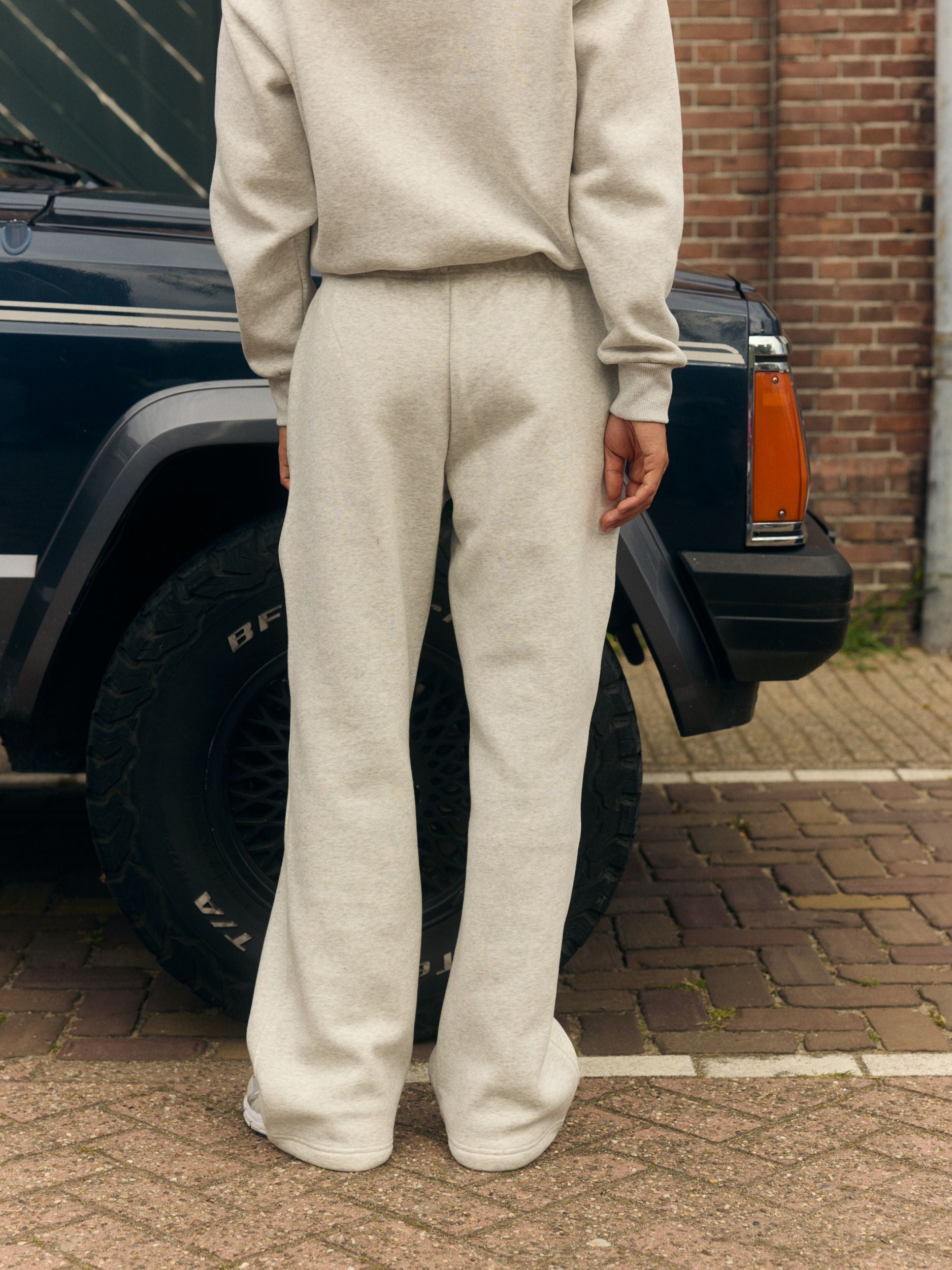 Woman wearing grey melange straight-leg sweatpants, seen from behind next to a vintage car.